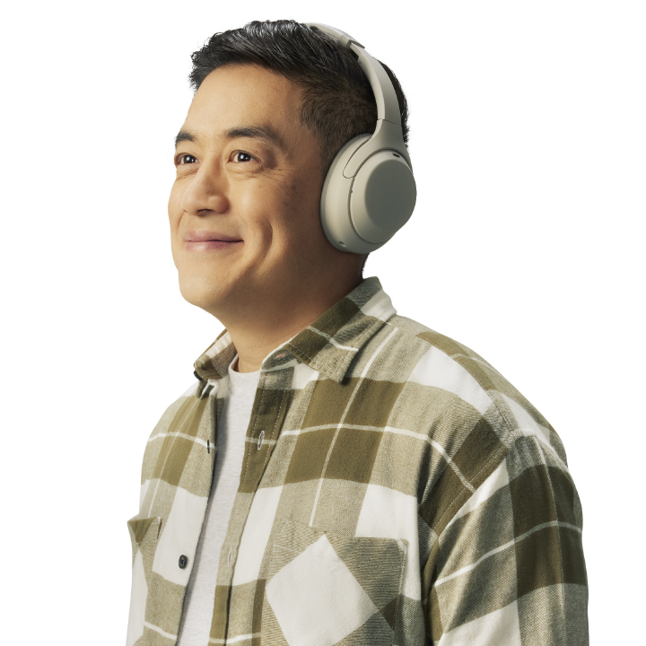 middle aged asian male with headphones walking and smiling